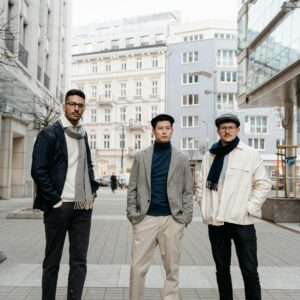 Three men in stylish attire posing confidently in an urban cityscape.